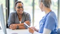 A patient talking with a doctor that is taking notes at a computer